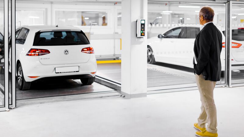 A man stands in front of a parking system with cars